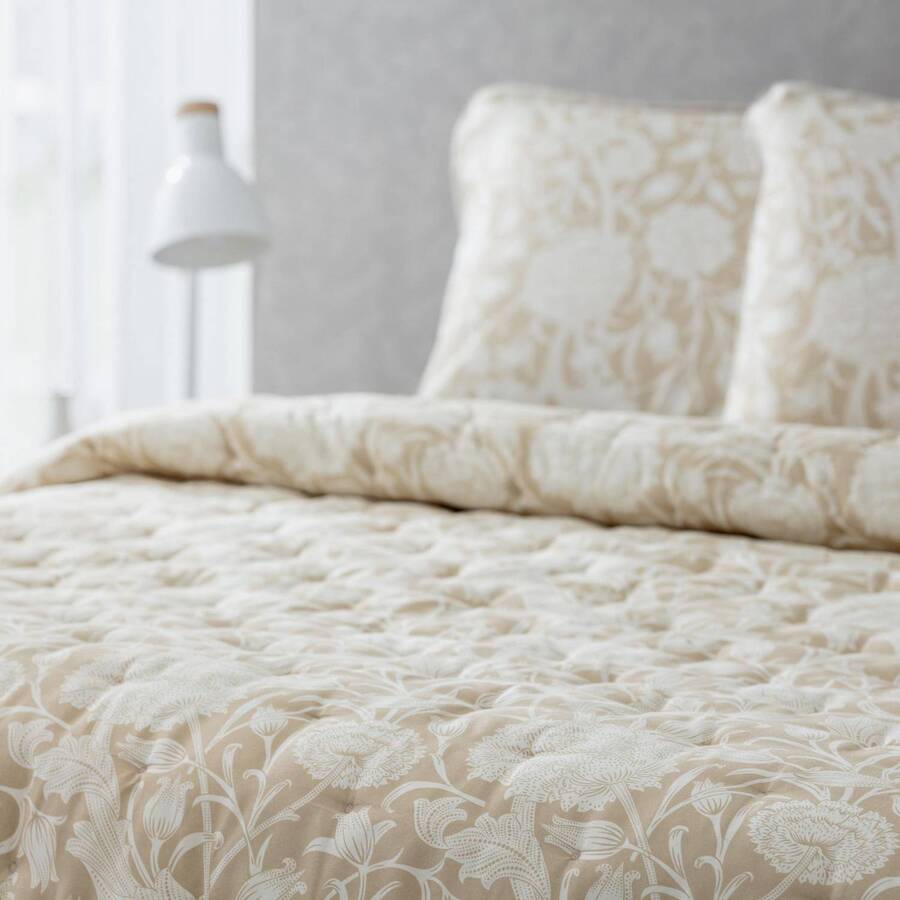 Detalle de cama, con plumón acolchado, con flores en color beige, estilo vintage. Dos almohadas del mismo estilo.