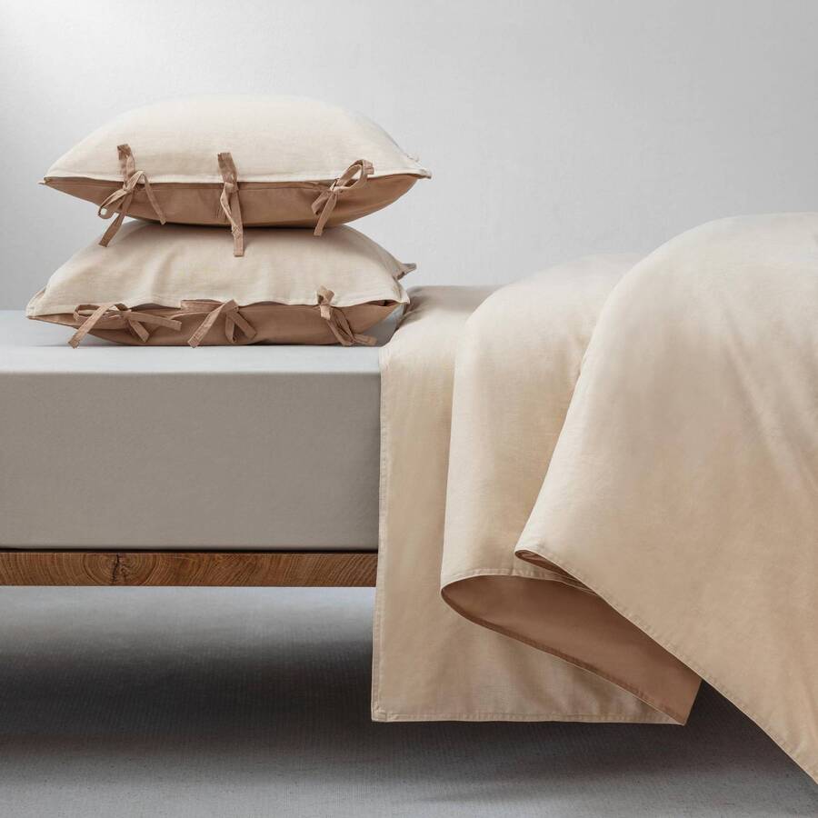 Cama de madera, con cubre plumón de lino en color beige. Dos almohadas con fundas de lino con amarres a los costados.