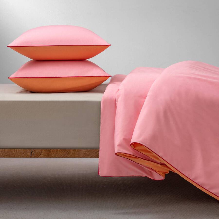Cama de madera con funda de plumón de color rosado y naranjo. Almohadas con fundas rosadas con naranjo.
