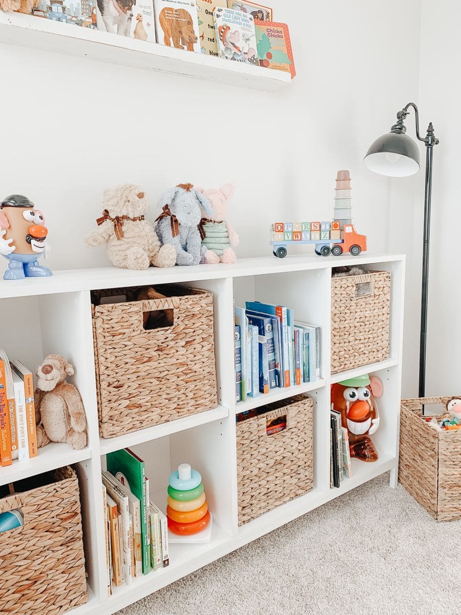 Pieza Montessori con un estante blanco con varios espacios para guardar. Además de libros y juguetes, hay canastos de fibra natural con más juguetes.
