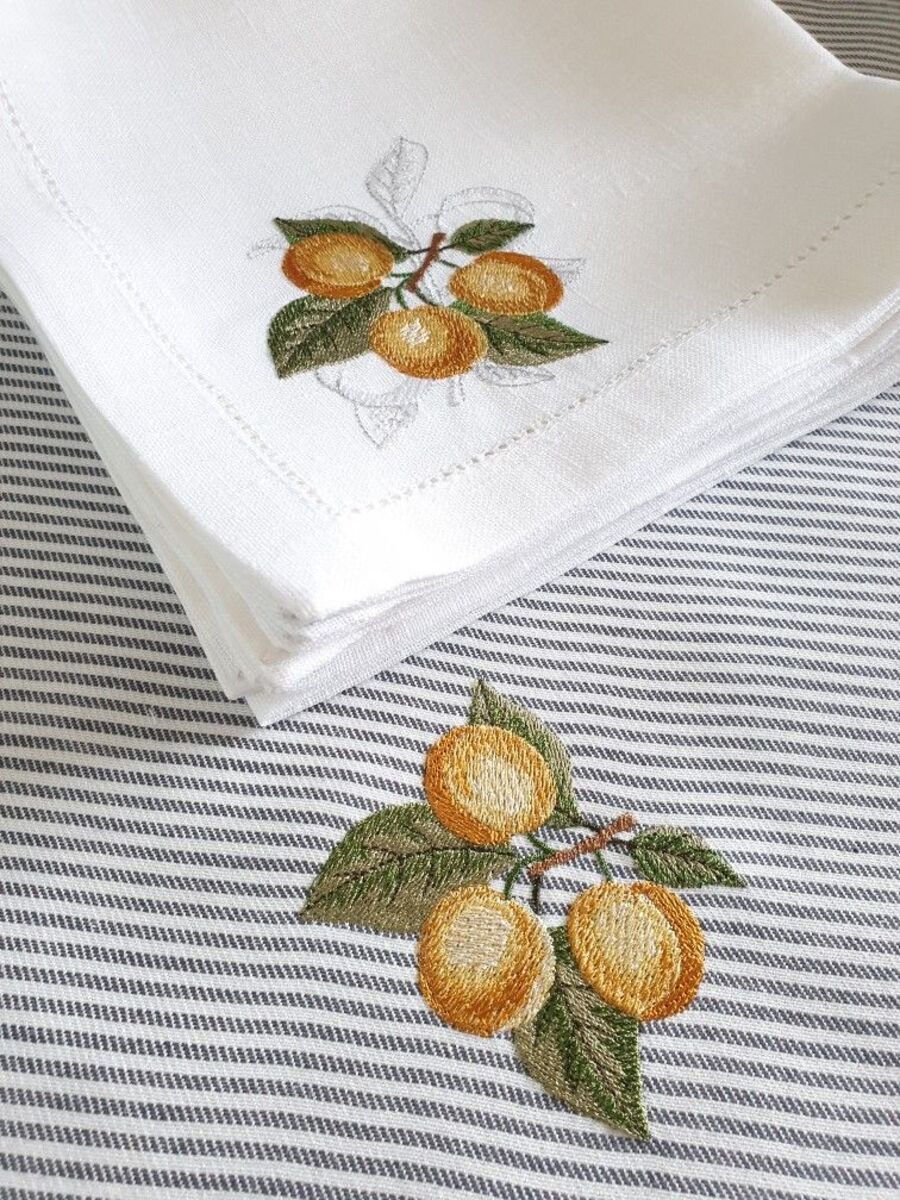 Detalle de mantel con rayas blanco con negro bordado con frutos de color amarillo. Sobre él, hay una servilleta de tela color blanca, también bordada con frutos amarillos.