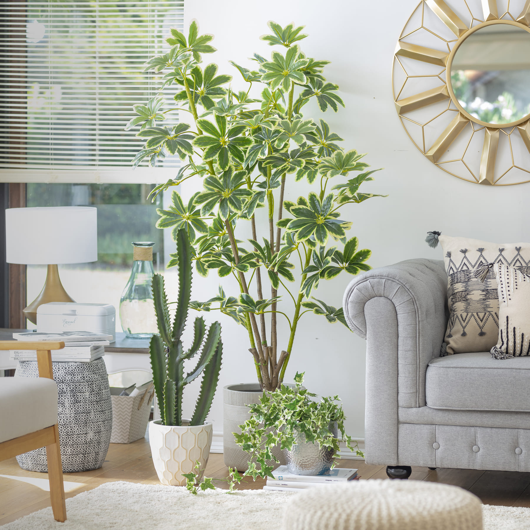 Sala de estar con un sofá gris con respaldo estilo capitoné y una poltrona gris con patas de madera. Entre ellas hay varias macetas grises y blancas con diferentes plantas.
