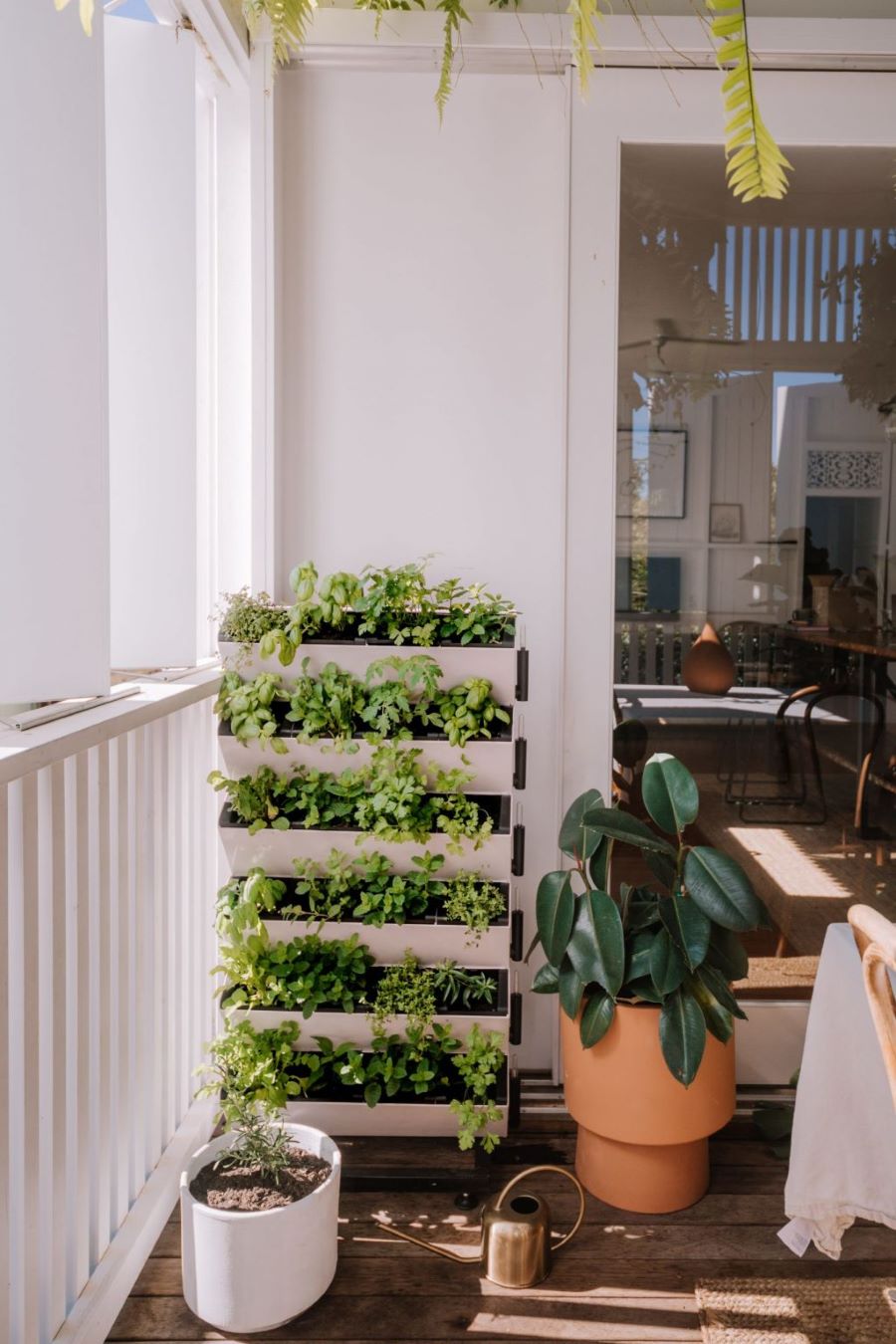 Terraza con mini huerto en carro con ruedas, con 6 repisas con hierbas y plantas. Junto al carro hay un macetero de arcilla con una planta y, delante, otro macetero blanco con plantas.