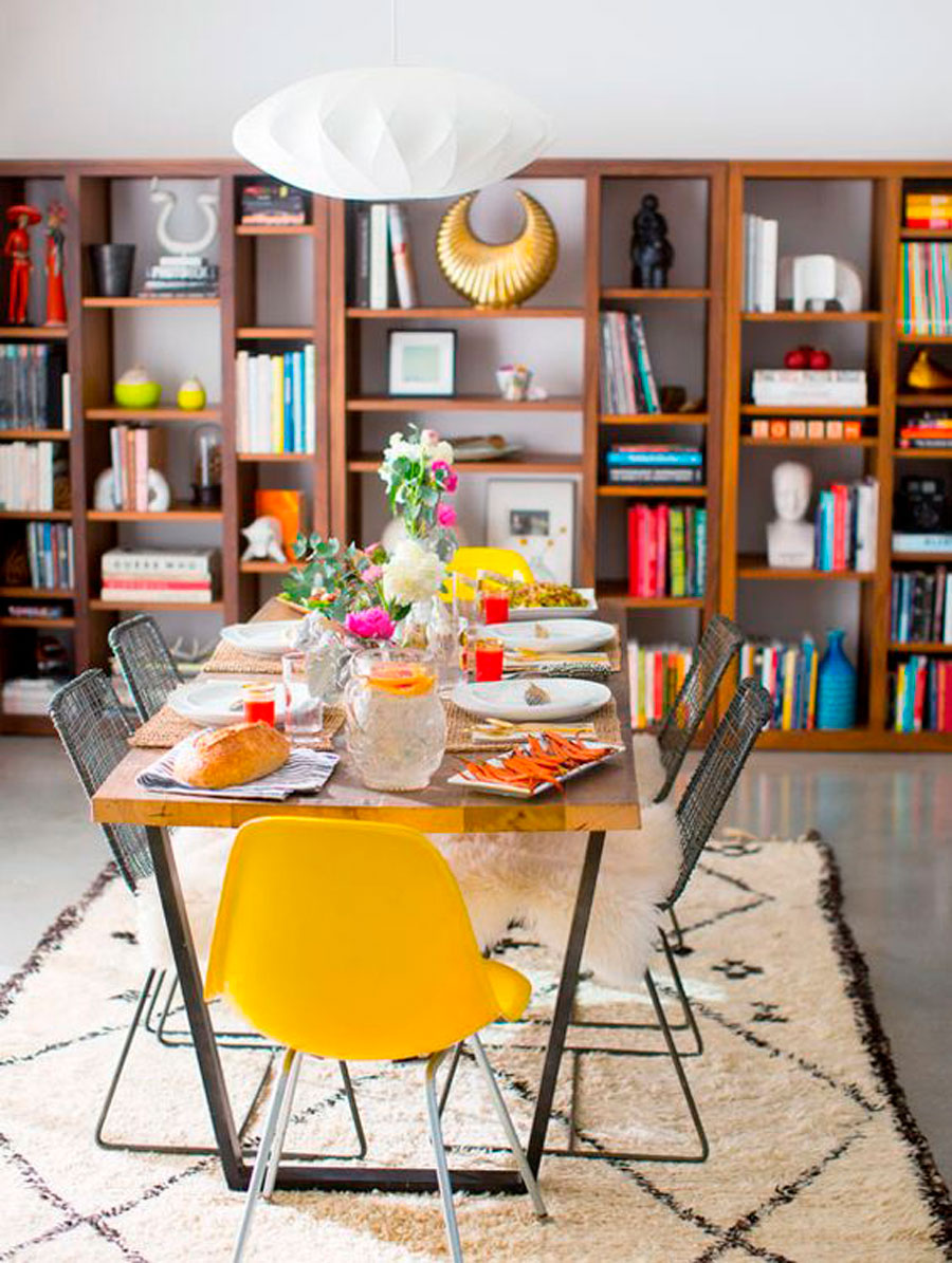 mesa de comedor de madera con sillas de colores y estante con libros