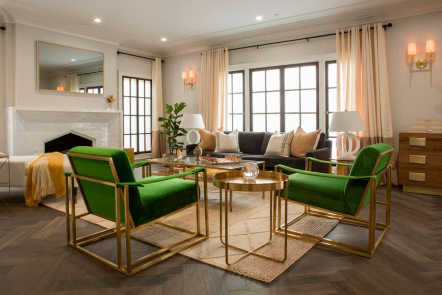 Living de Drew Scott con alfombra color crema, muebles con estructura dorada, vidrio y tapices verdes de terciopelo