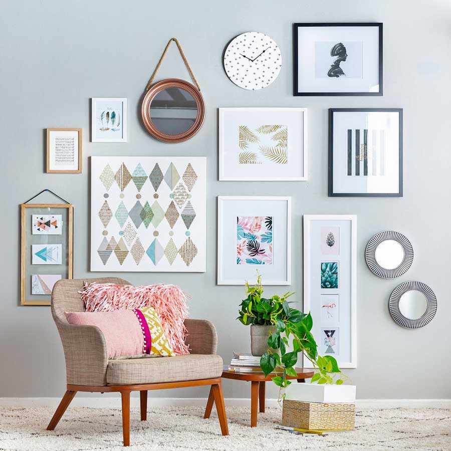 Espacio de la casa con un muro galería, una poltrona beige con cojines rosados y una mesa lateral de madera con una planta y revistas.
